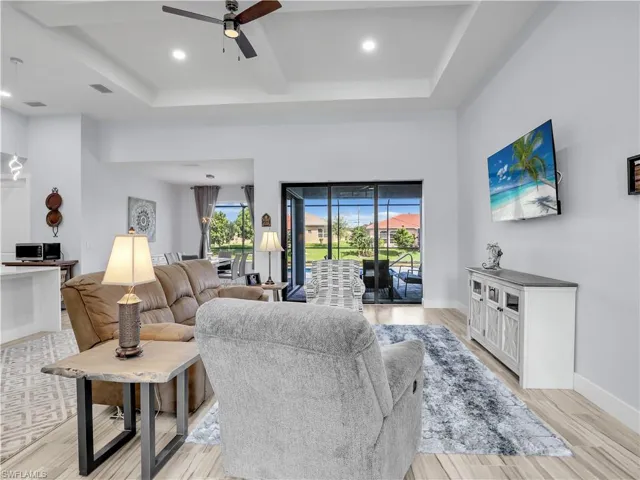 Living room featuring light wood-type flooring, ceiling fan, and a tray ceiling