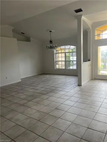 Unfurnished living room with ornate columns, a chandelier, light tile flooring, and crown molding