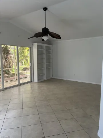 Tiled spare room featuring vaulted ceiling, ornamental molding, and ceiling fan
