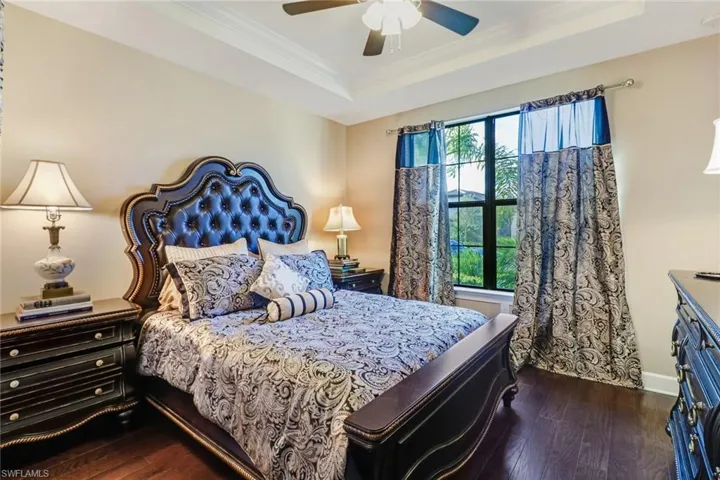 Bedroom with ornamental molding, a tray ceiling, dark wood-style floors, and a ceiling fan