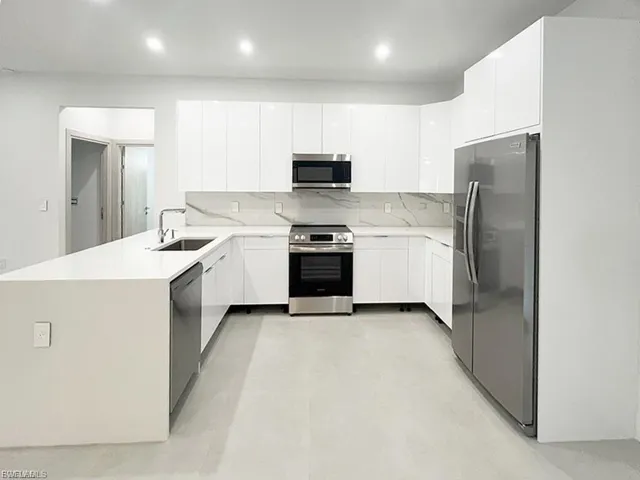 Kitchen with appliances with stainless steel finishes, a peninsula, tasteful backsplash, modern cabinets, and light countertops