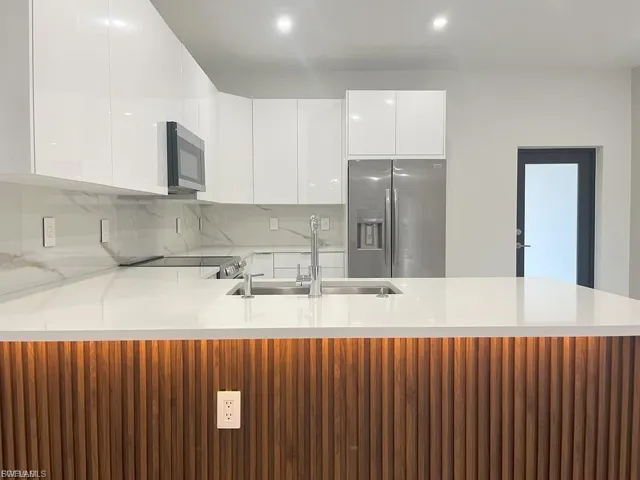 Kitchen featuring modern cabinets, appliances with stainless steel finishes, white cabinets, light countertops, and a peninsula