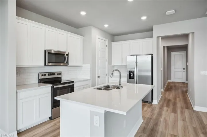 Kitchen featuring light hardwood / wood-style flooring, a center island with sink, stainless steel appliances, and white cabinetry
