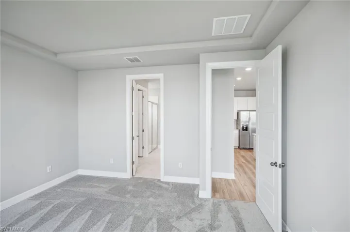 Unfurnished bedroom featuring stainless steel refrigerator with ice dispenser and light carpet