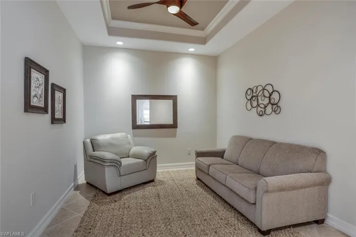 Living room with a raised ceiling, crown molding, tile patterned flooring, and ceiling fan
