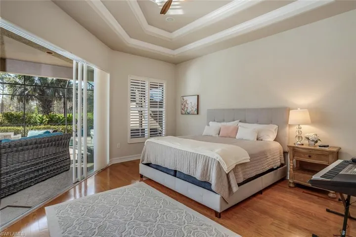 Bedroom featuring wood-type flooring, access to outside, crown molding, and a tray ceiling