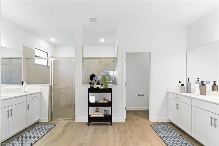 Bathroom featuring a shower with shower door, wood style flooring and his/her vanities