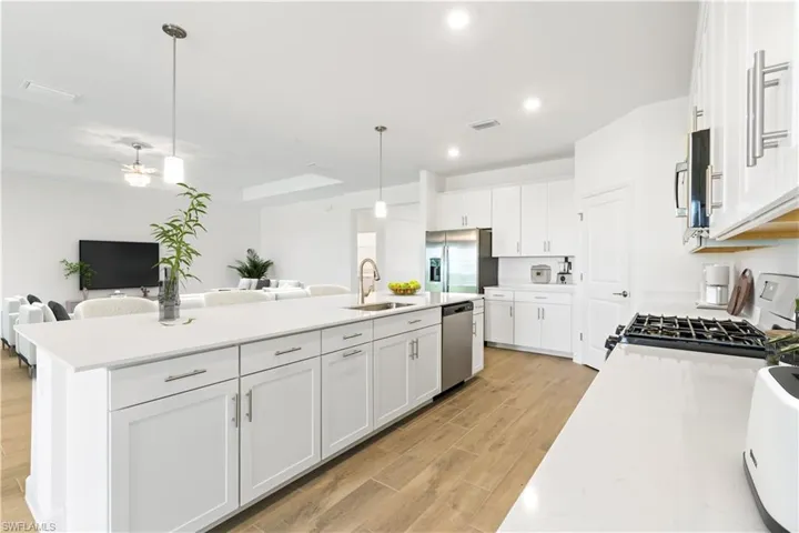 Kitchen featuring an island with sink, white cabinetry, wood style flooring and stainless steel appliances