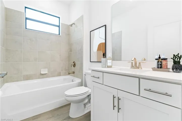 Full bathroom featuring tiled shower / bath, toilet, vanity with extensive cabinet space, and wood style flooring