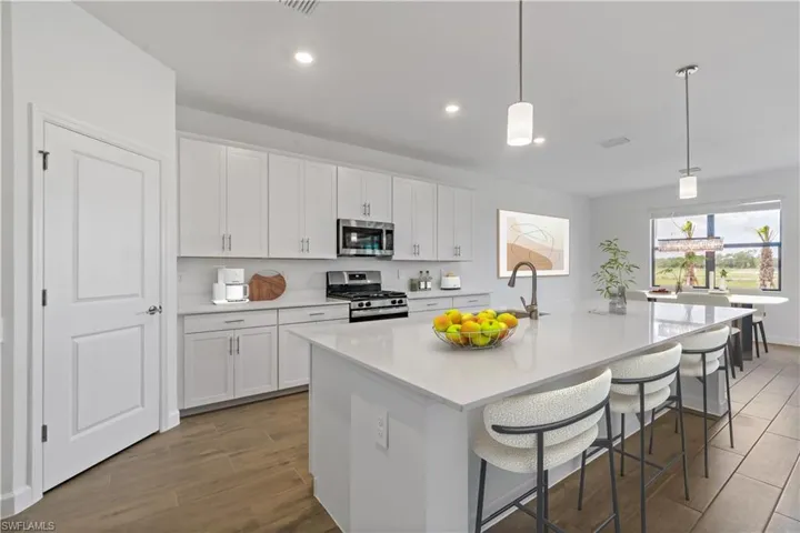 Kitchen featuring wood style floors, an island with sink, pendant lighting, white cabinets, and appliances with stainless steel finishes