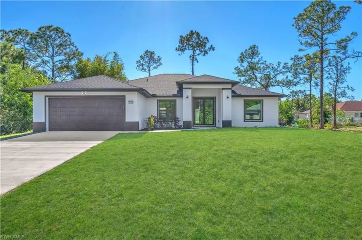 Prairie-style home with stucco siding, a front lawn, driveway, an attached garage, and roof with shingles