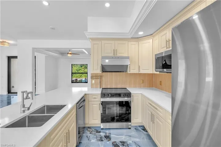 Kitchen featuring appliances with stainless steel finishes, light marble finish floors, cream cabinets, light stone counters, and under cabinet range hood