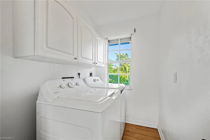 Washroom with light wood-style floors, cabinet space, washing machine and clothes dryer, and a textured wall