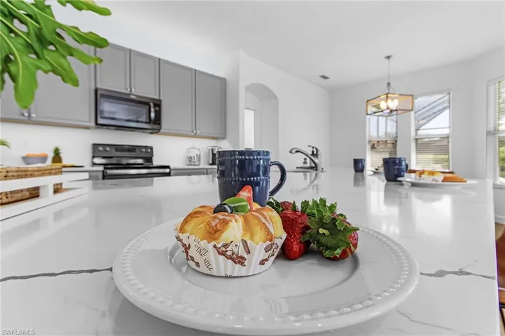 Kitchen featuring light stone countertops, decorative light fixtures, gray cabinetry, and stainless steel microwave