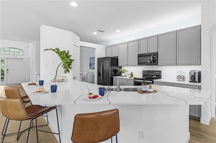 Kitchen featuring gray cabinetry, a breakfast bar, black appliances, light stone counters, and recessed lighting