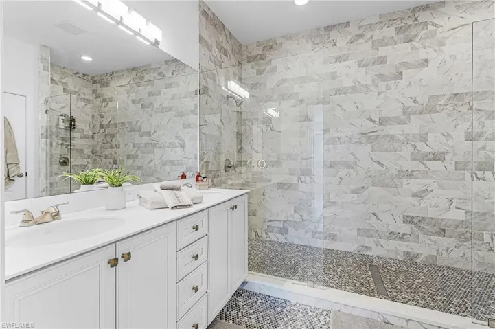 Bathroom with walk in shower, double vanity, tile walls, recessed lighting, and light tile patterned floors
