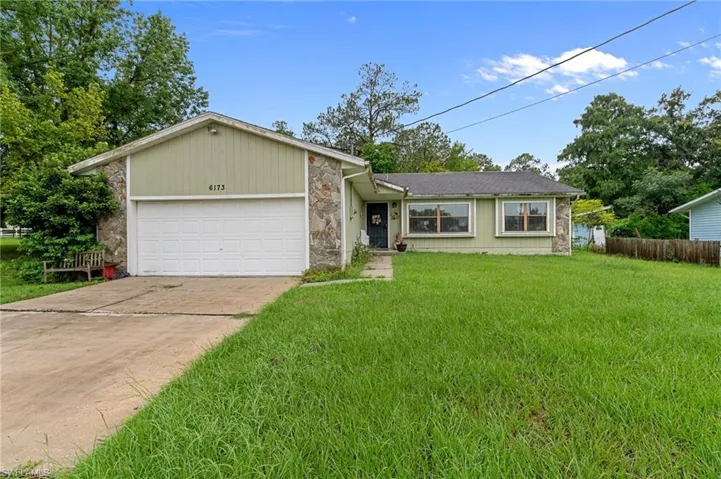 Front exterior featuring stone facade accents, light green siding, and an attached garage with a concrete driveway