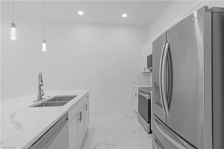 Kitchen featuring stainless steel appliances, light marble finish flooring, white cabinetry, hanging light fixtures, and light stone counters
