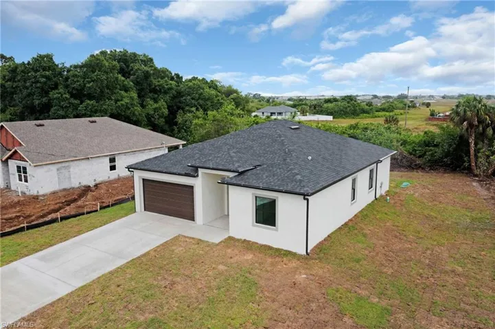 View of front facade with stucco siding, driveway, a garage, a front yard, and a shingled roof