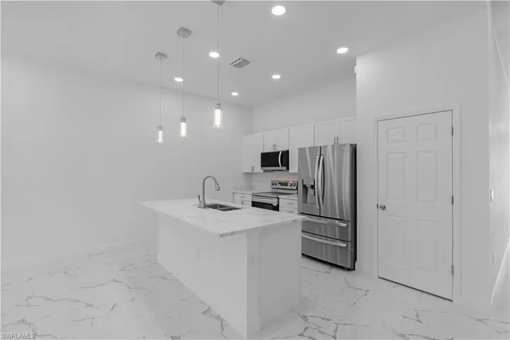 Kitchen with light marble finish floors, appliances with stainless steel finishes, white cabinets, light stone counters, and recessed lighting