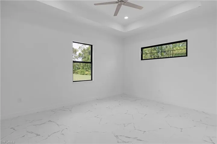 Empty room with plenty of natural light, a tray ceiling, marble look tiles, recessed lighting, and ceiling fan