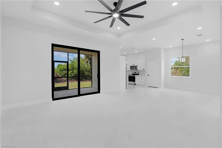 Unfurnished living room featuring healthy amount of natural light, recessed lighting, a raised ceiling, and ceiling fan
