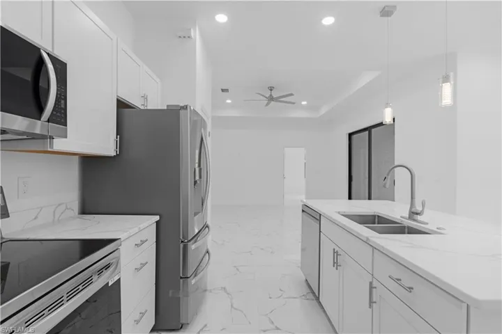Kitchen featuring appliances with stainless steel finishes, light marble finish flooring, recessed lighting, white cabinets, and decorative light fixtures