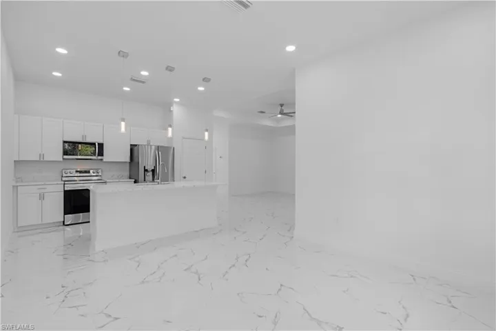 Kitchen featuring light marble finish flooring, appliances with stainless steel finishes, white cabinets, light countertops, and open floor plan