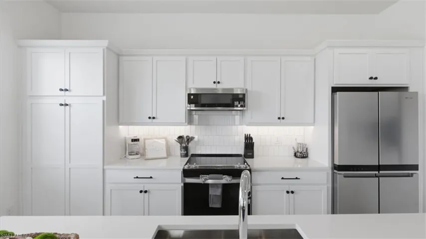 Kitchen with stainless steel appliances, white cabinets, tasteful backsplash, and light stone counters - Virtually Edited