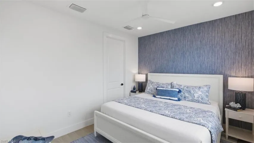 Bedroom with an accent wall, wallpapered walls, a ceiling fan, recessed lighting, and wood finished floors - Virtually Edited