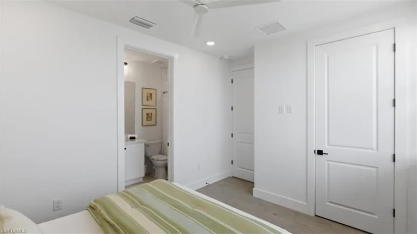Bedroom with light wood-type flooring, ensuite bathroom, and recessed lighting - Virtually Edited