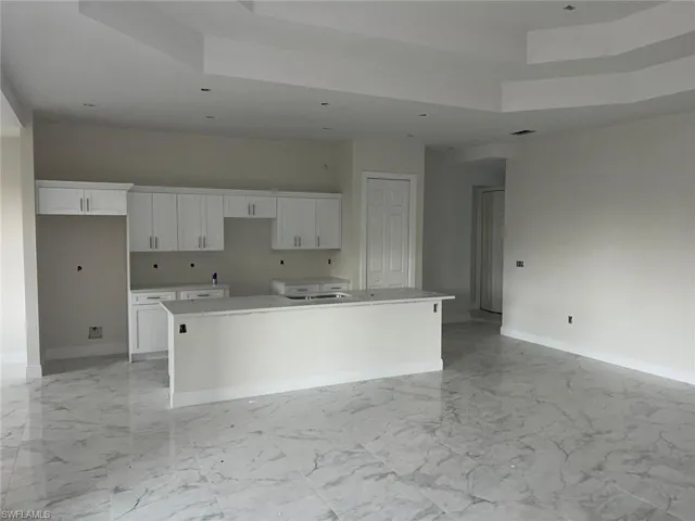 Kitchen with sink, a tray ceiling, light tile patterned floors, white cabinets, and a kitchen island