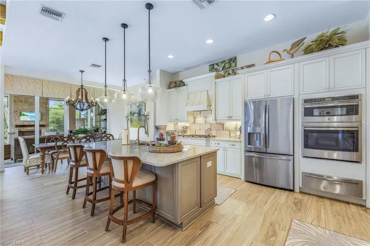 Kitchen featuring light hardwood / wood-style floors, stainless steel appliances, an island with sink, decorative light fixtures, and a notable chandelier