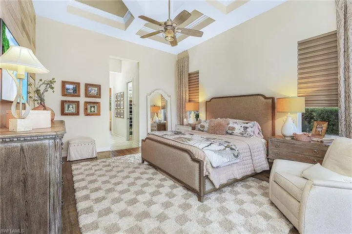 Bedroom with beam ceiling, a towering ceiling, coffered ceiling, ensuite bathroom, and ceiling fan