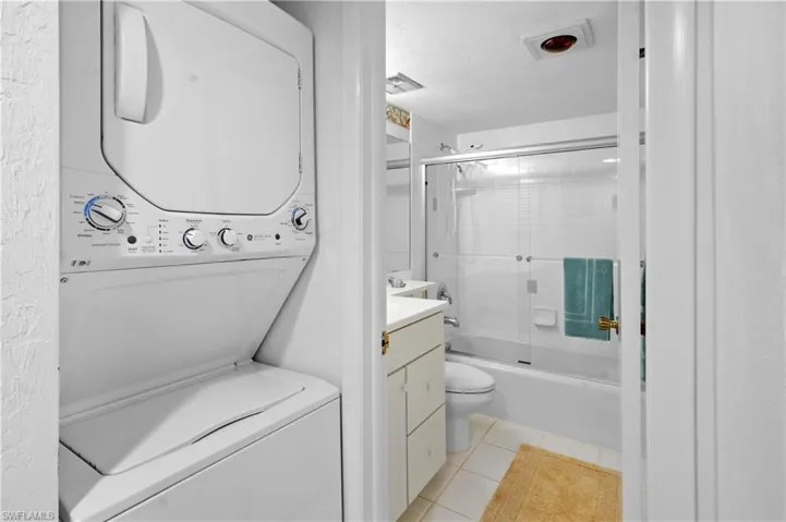 Full bath featuring vanity, stacked washer and dryer, tile patterned floors, toilet, and combined bath / shower with glass door