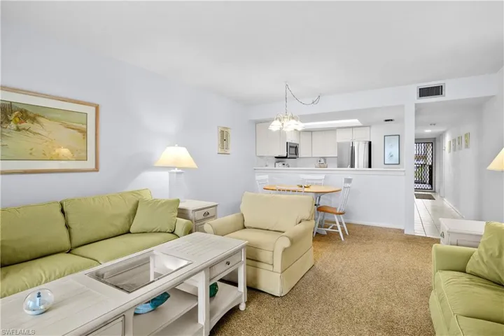 Living room featuring a notable chandelier, visible vents, and light colored carpet