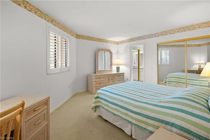 Bedroom featuring a closet, baseboards, light colored carpet, and ensuite bath