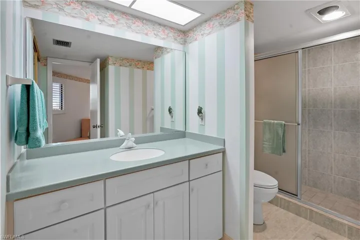 Bathroom with visible vents, wallpapered walls, toilet, a stall shower, and a skylight