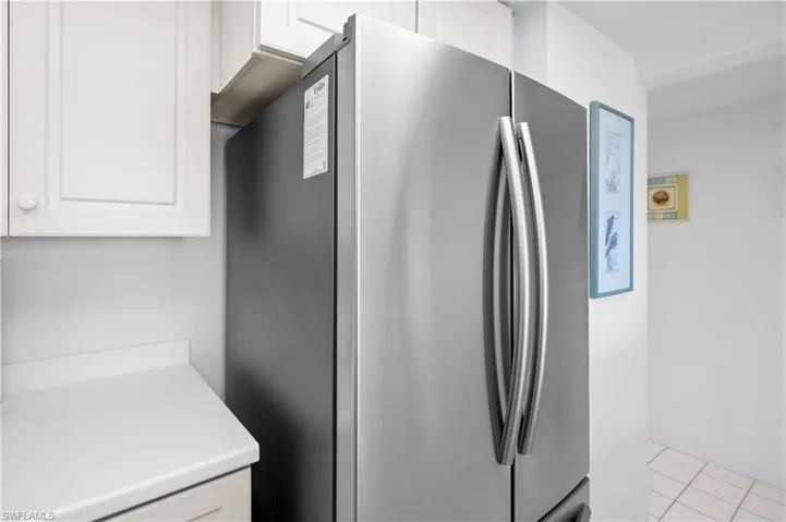 Kitchen featuring white cabinetry, light tile patterned flooring, light countertops, and freestanding refrigerator