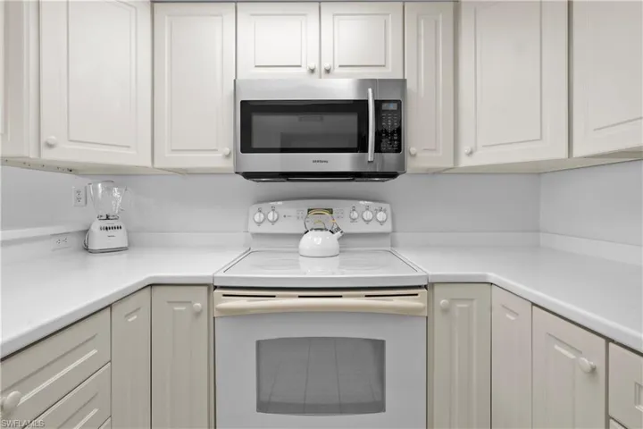 Kitchen featuring stainless steel microwave, white cabinets, light countertops, and white range with electric cooktop