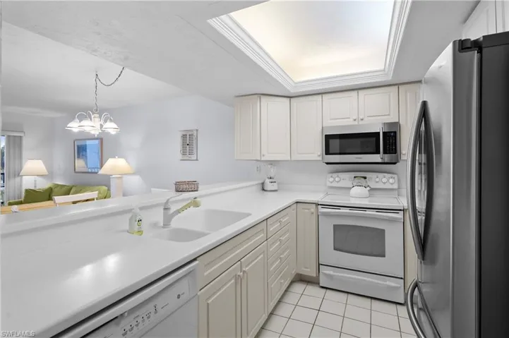 Kitchen with light tile patterned floors, appliances with stainless steel finishes, white cabinets, a raised ceiling, and a sink
