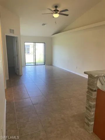 Empty room with lofted ceiling, a ceiling fan, and light tile patterned flooring