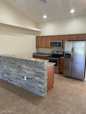 Kitchen with stainless steel appliances, brown cabinets, recessed lighting, and light tile patterned floors