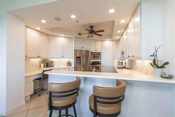 Kitchen with breakfast bar, white cabinetry, desk area, and stainless appliances