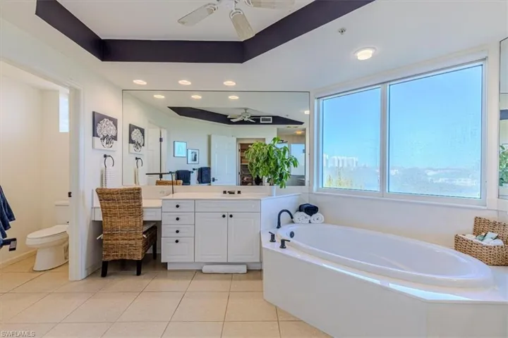 Master bathroom featuring plenty of natural light, separate vanities, tray ceiling, and large garden tub