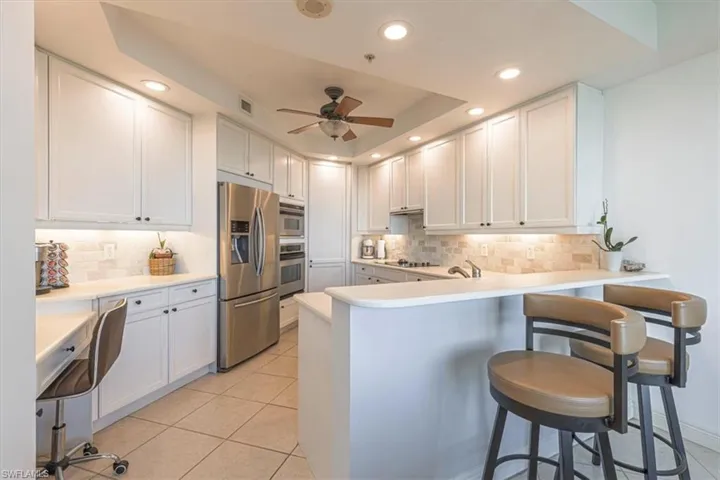 Kitchen featuring a breakfast bar area, white cabinetry, appliances with stainless steel finishes, tray ceiling, and a desk area