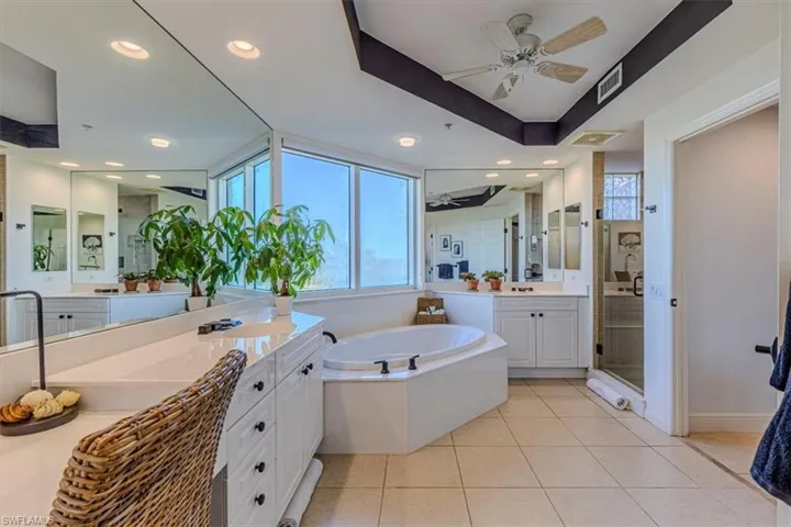 Master Bathroom with a garden tub, glass enclosed shower, two separate vanities, recessed lighting, updated fixtures, and tray ceilings
