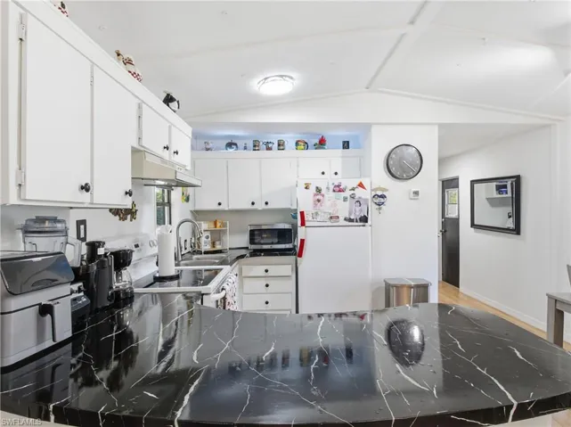 Kitchen with vaulted ceiling, white cabinetry, white appliances, under cabinet range hood, and light wood-type flooring