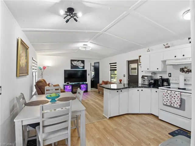 Kitchen featuring electric range, light wood-style flooring, white cabinets, lofted ceiling, and a peninsula