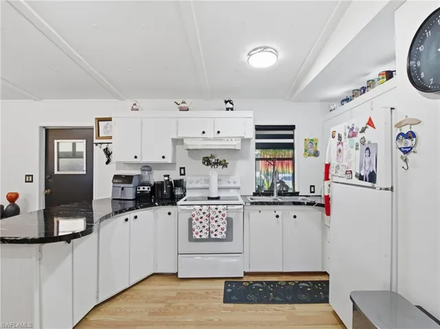 Kitchen featuring white appliances, light wood finished floors, white cabinetry, a peninsula, and beamed ceiling